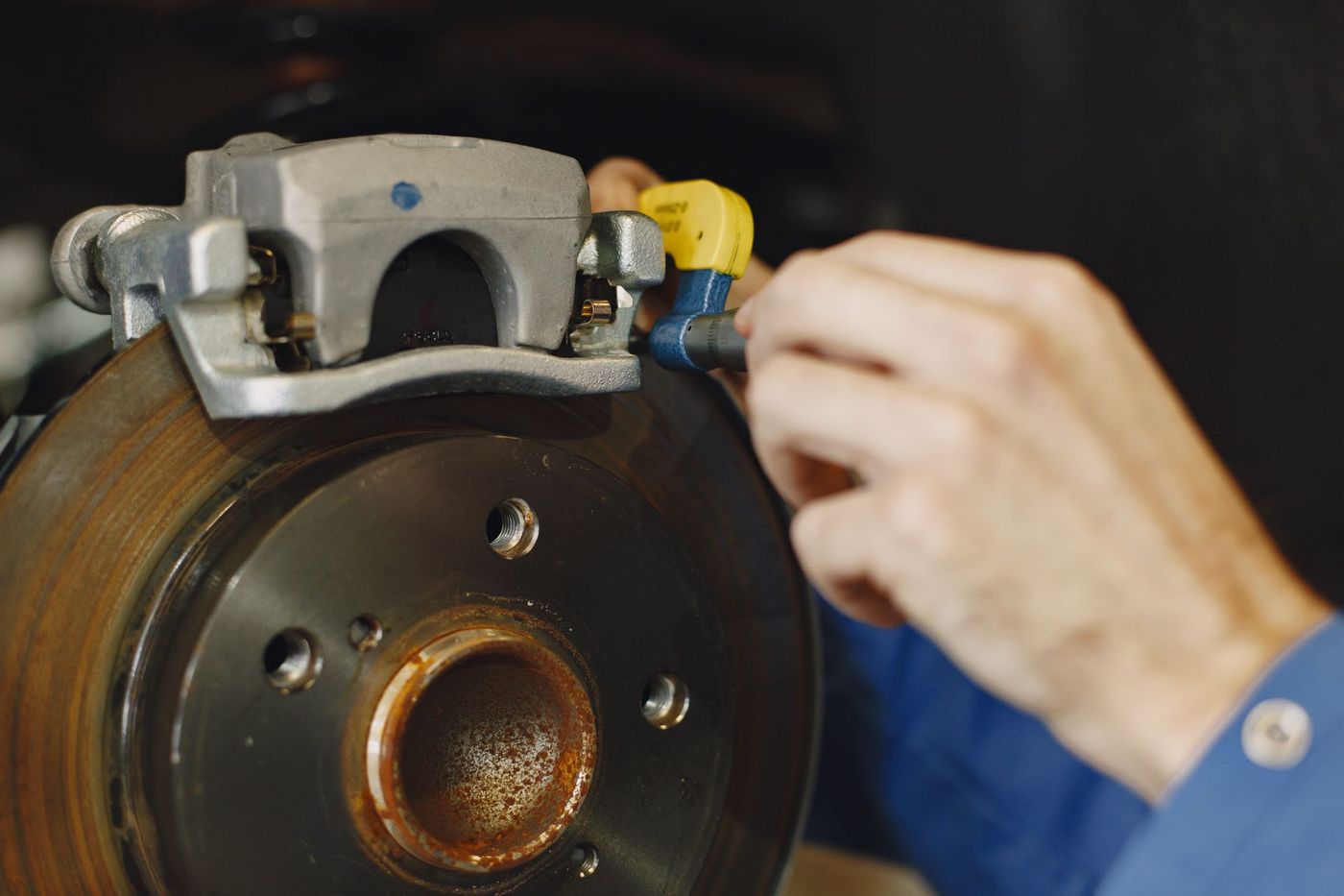A gloved hand working at a vehicle disc brake and caliper with the wheel removed