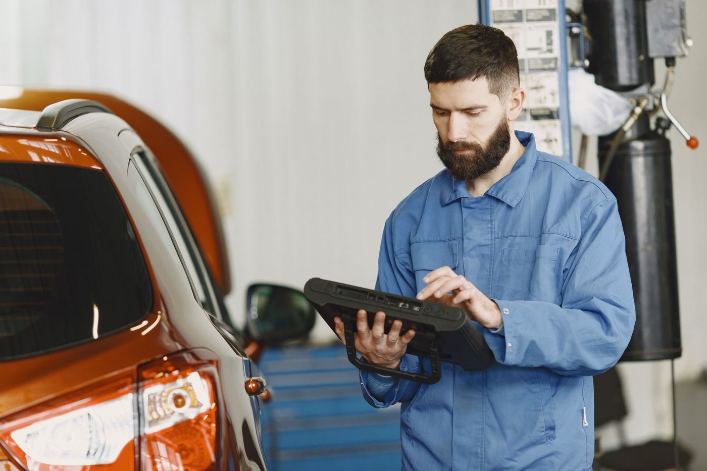 A technician reading a handheld automotive diagnostic tool beside a car