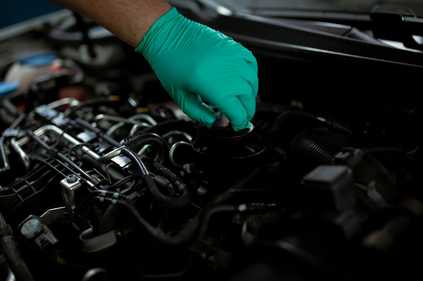 A gloved hand opening the oil filler cap on a car engine