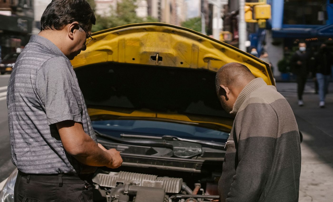 Two people looking under the raised hood of a car at the roadside